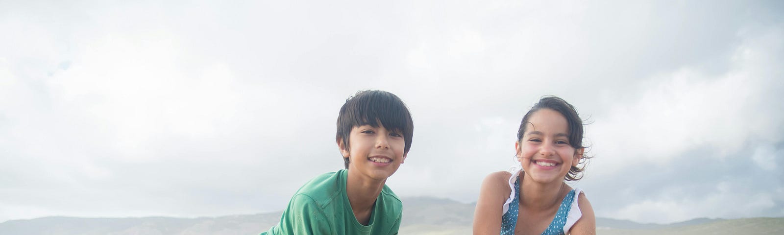 Young boy and girl digging hole in sand at beach, grinning at the viewer