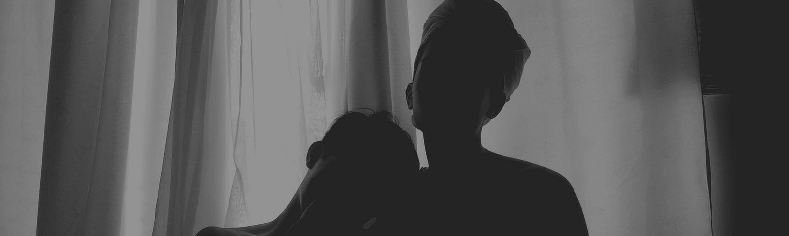 A black and white of two people’s silhouettes in front of a curtained window.