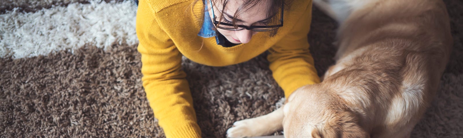 Woman on the computer lying on a rug with dog next to her.