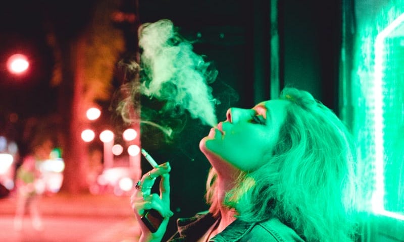 Neon light blonde woman smoking at night.