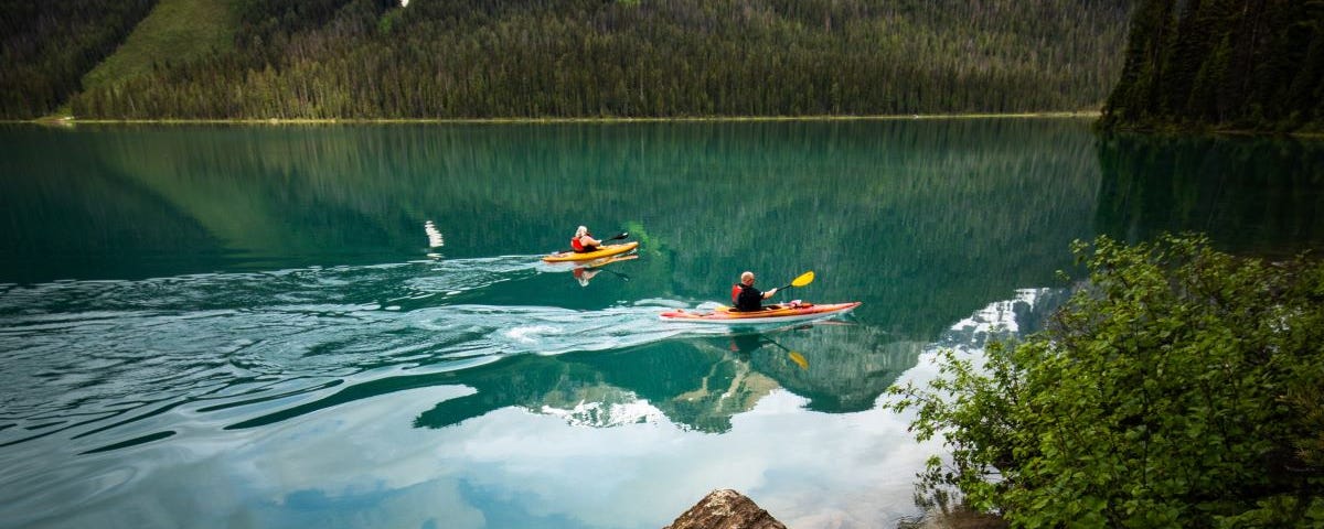 Two people kayaking on a scenic mountain-ringed lake.