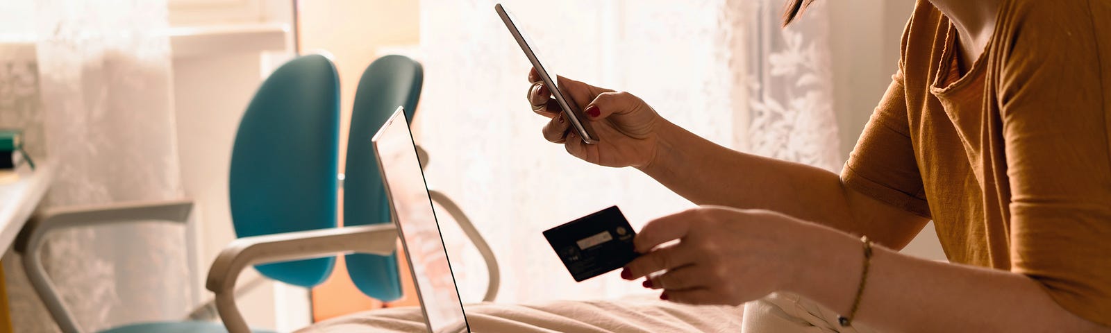 Woman holding credit card and looking at phone as she online shops.