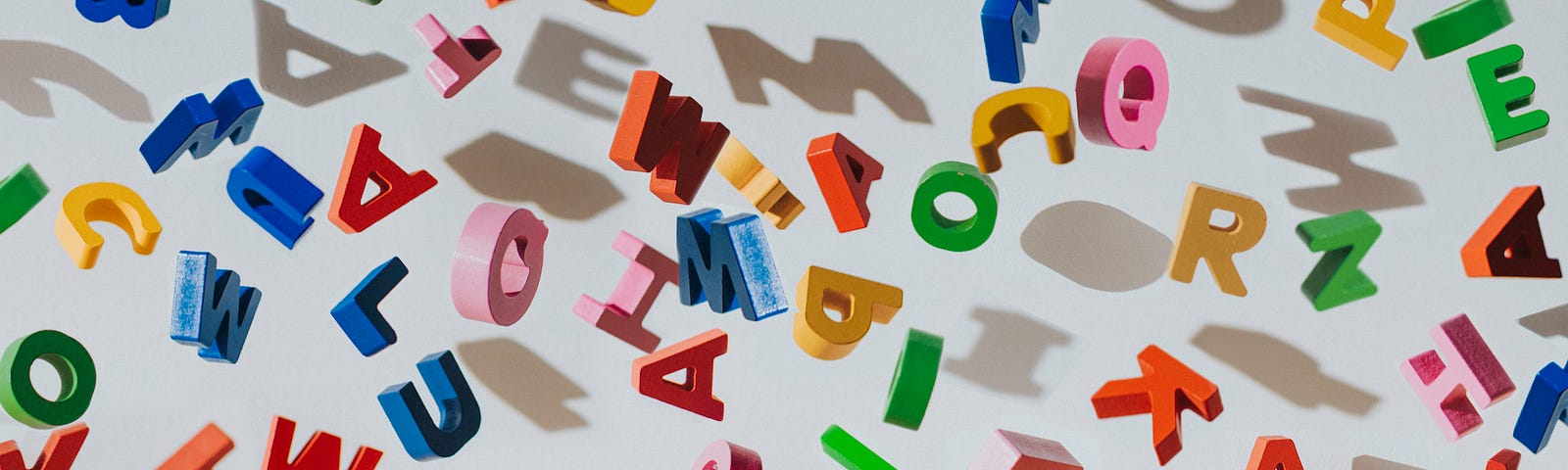 Conceptual image of colourful falling letters, casting shadows on a white wall.