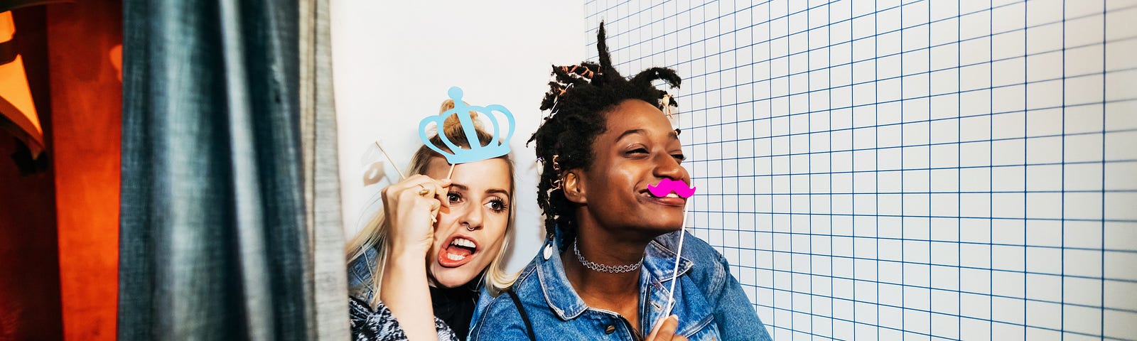 Two friends taking pictures and messing about with accessories in a photo booth on a night out together.