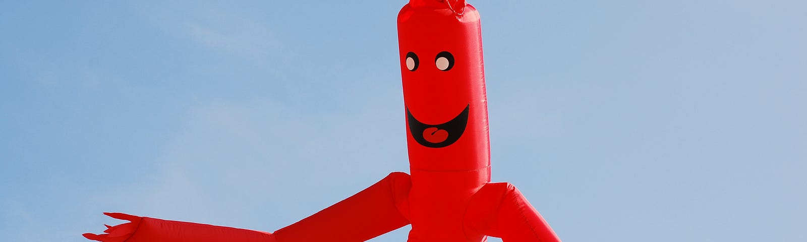 A photo of a red inflatable tube man against a clear blue sky.