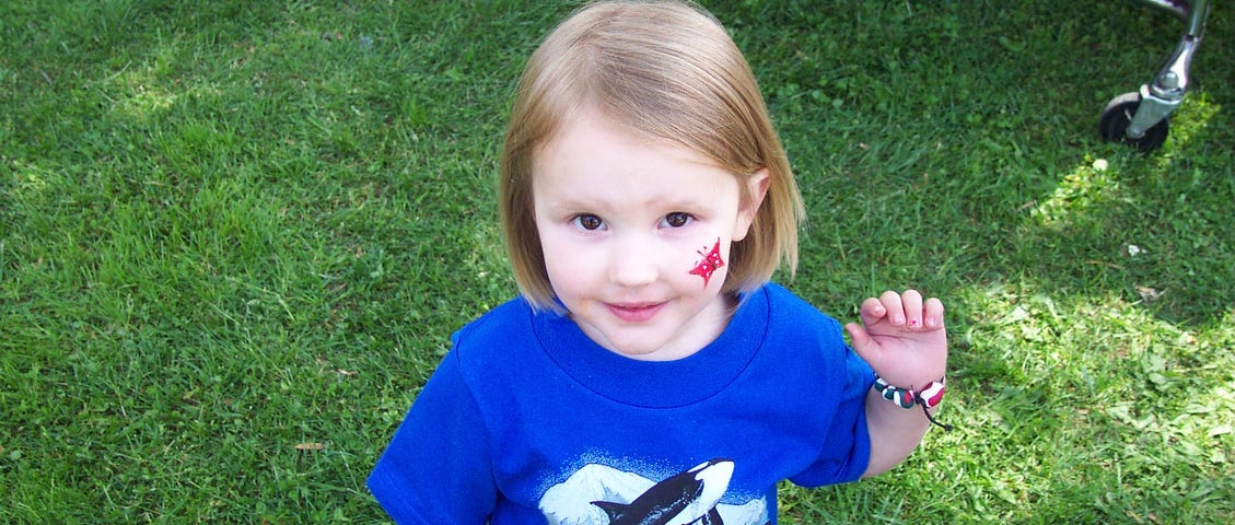 Photo of child in blue shirt with a red star tattoo on her face.