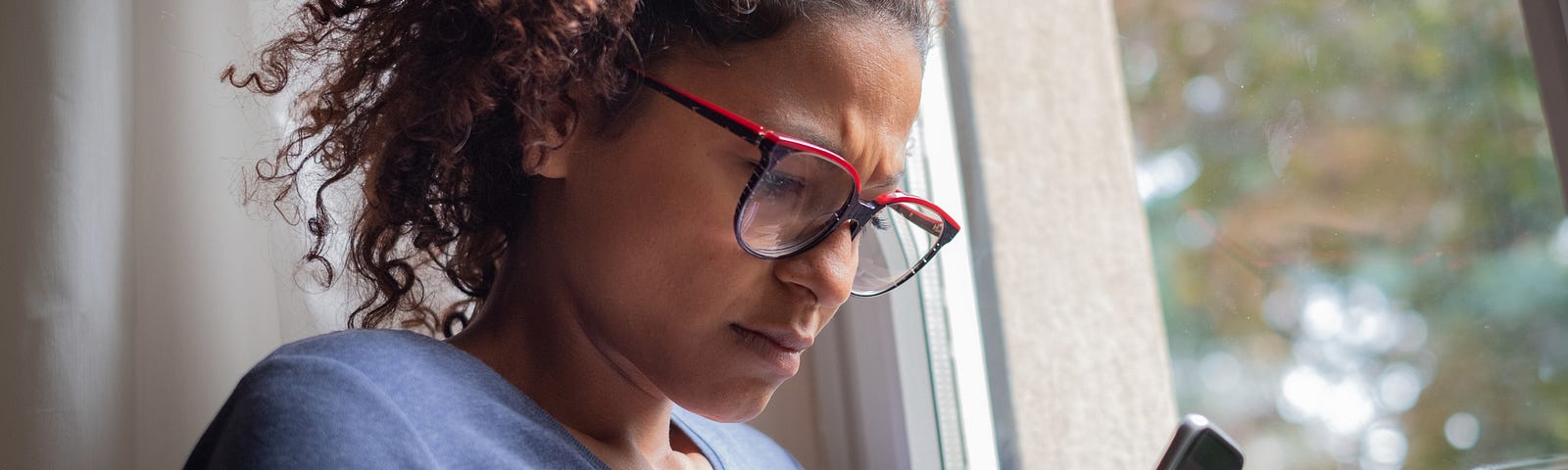 A photo of a black woman looking at her phone, looking upset.