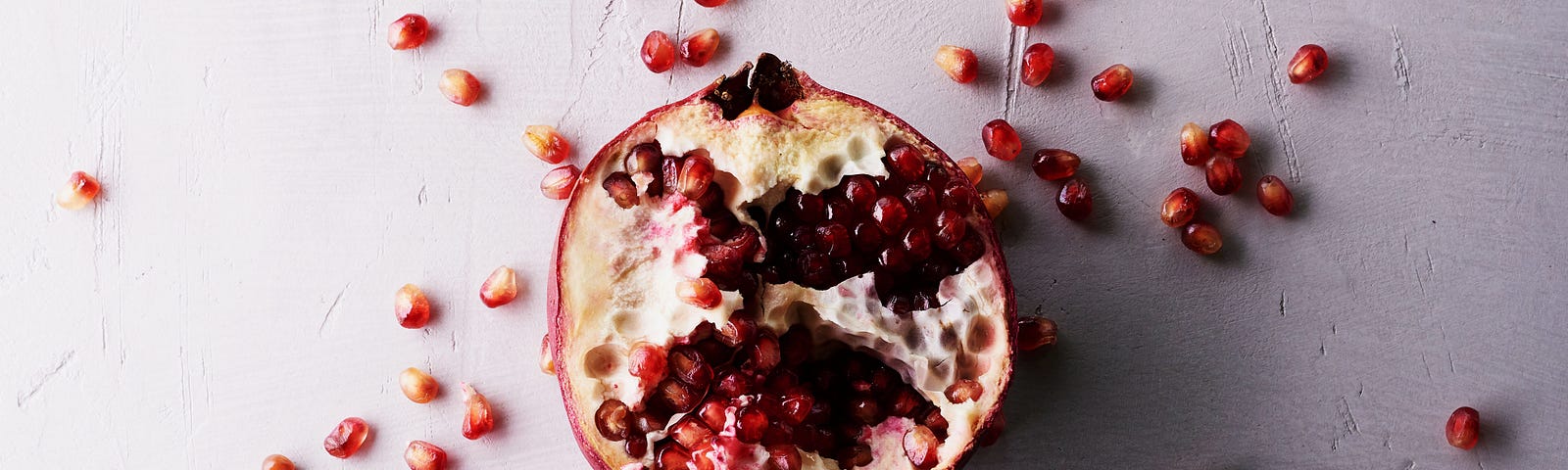 A halved pomegranate sitting on a marble surface, pips scattered around it.