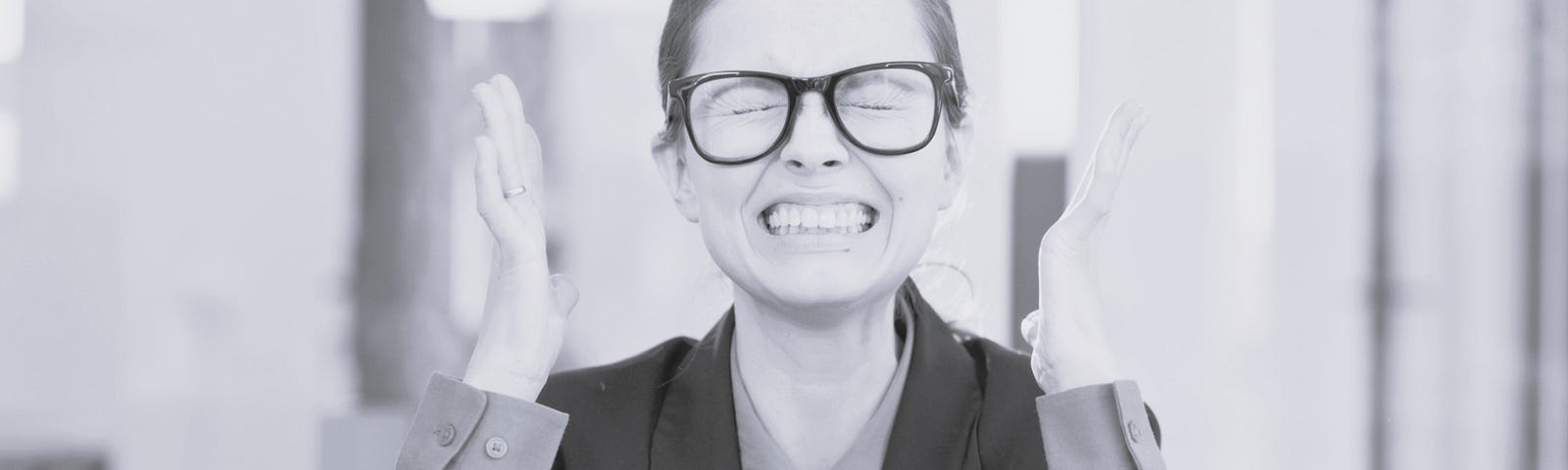 Woman in a suit and glasses with a grimace on her face and her hands held up as if she is completely dumfounded.