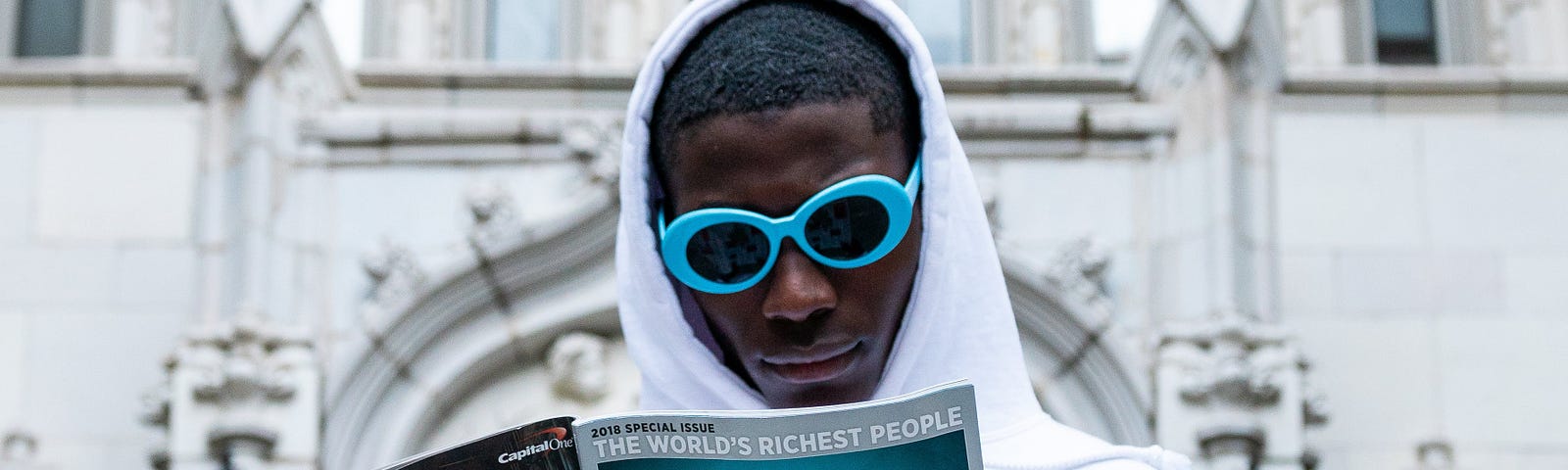 black man wearing light blue sunglasses and a white hoodie, reading Forbes