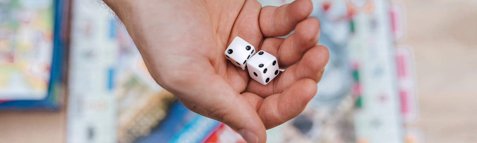 A hand holding two dice above a monopoly board game