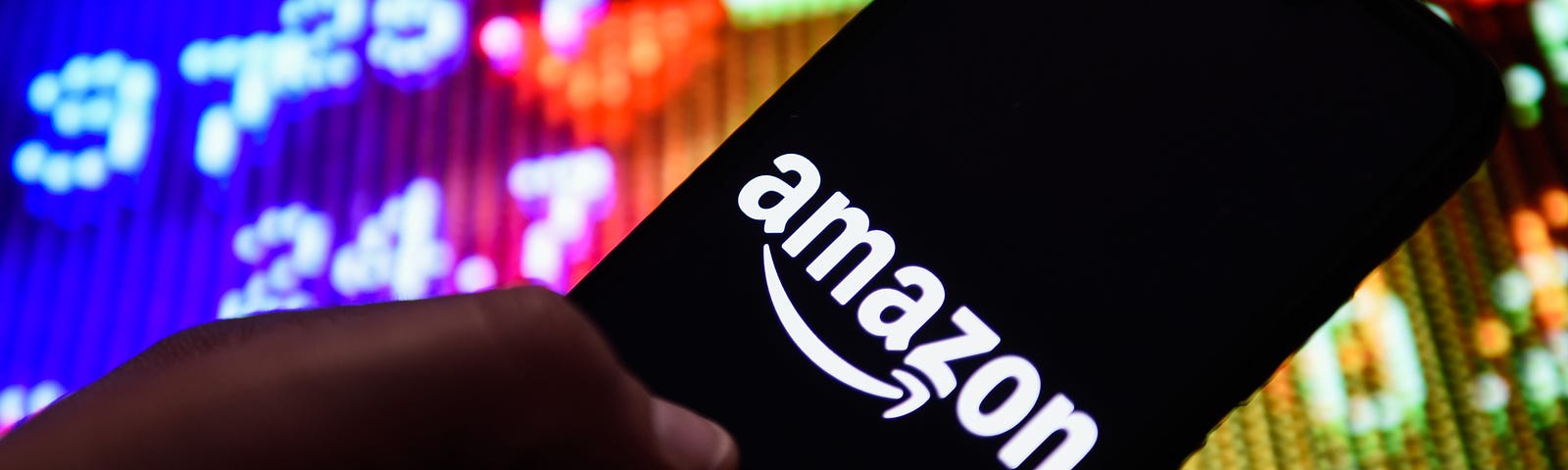 Photo illustration of the Amazon logo displayed on a smart phone against a colorful stock ticker backdrop.