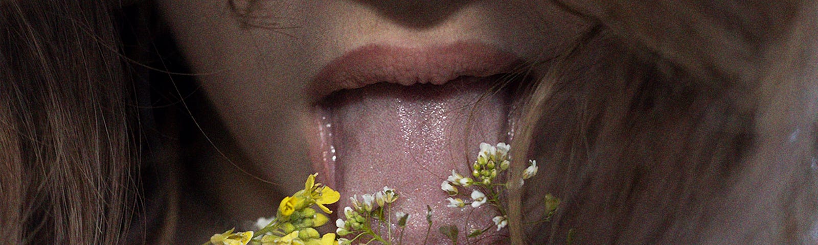 A woman, with her face partially hidden by her hair, is licking some flowers