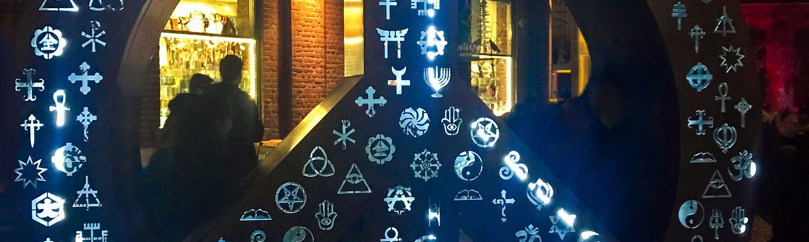 Symbolic Peace sculpture by artist, Michael Rosenblatt, 10-foot peace sign, with cultural and religious symbols illuminated at night | photography | pockett dessert