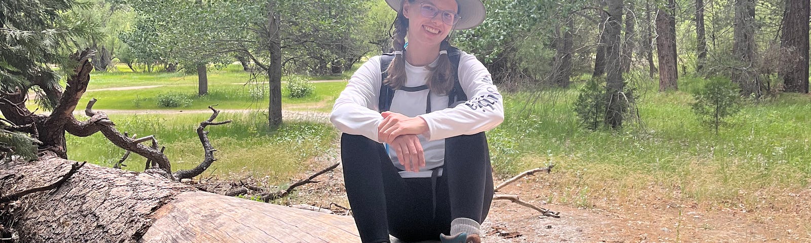 Me sitting on a fallen log, wearing a white shirt, black pants, and hiking boots
