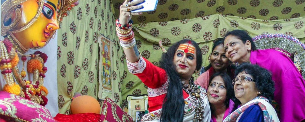 Laxmi Narayan Tripathi, a hijra with long hair and wearing makeup and a sari, takes a selfie with four women.