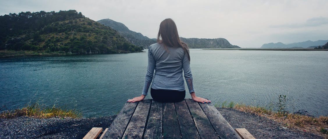 A woman sits on a pier overlooking a lake.