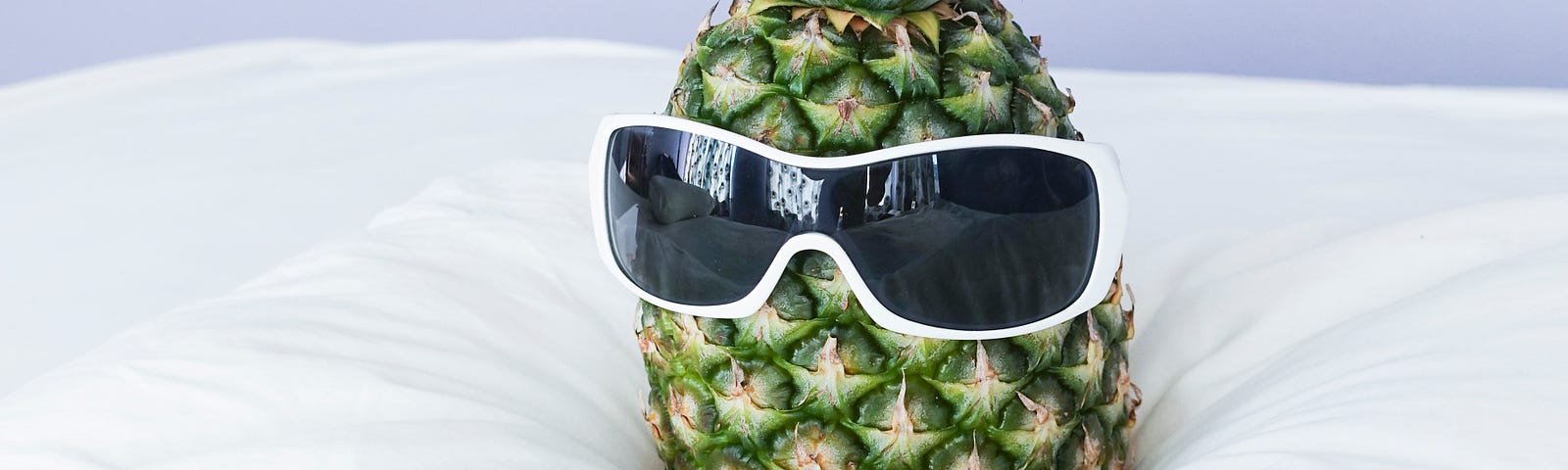 A pineapple sits comically on the bed, wearing sunglasses.