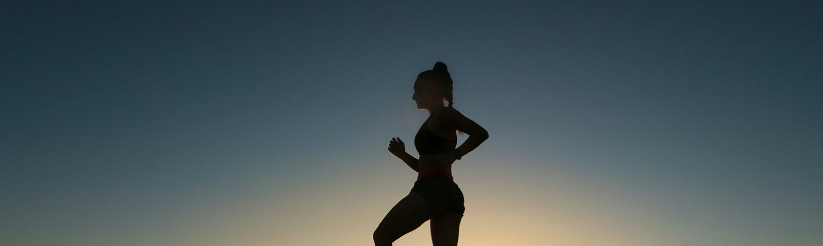 silhouette of a runner on a rocky ledge against a glowing sky