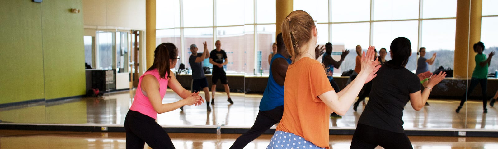 People are taking a dance class in which a mirror lines the front wall of the room. #dance #danceclass #zumba #dancers