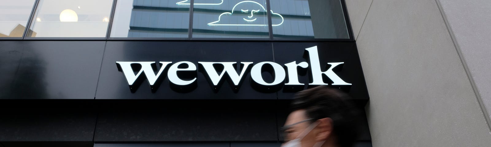 A man wearing a face mask walks past the front of a WeWork building in Tokyo.