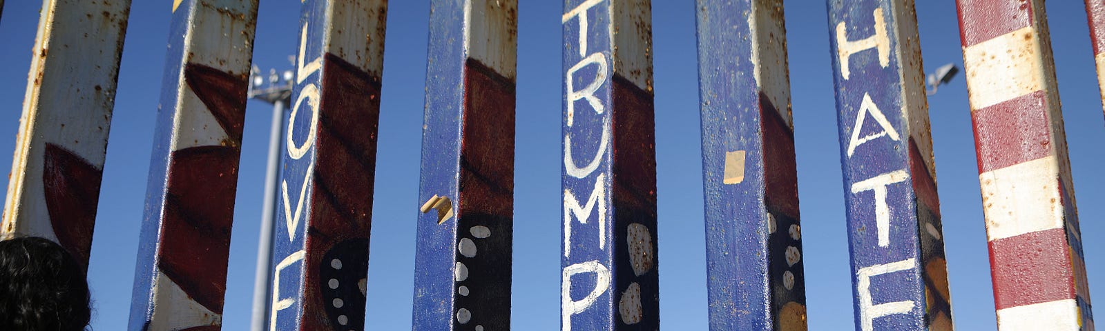 A girl stands beneath a painted message ‘Love Trumps Hate’ while looking towards the U.S. along the U.S.-Mexico border fence.