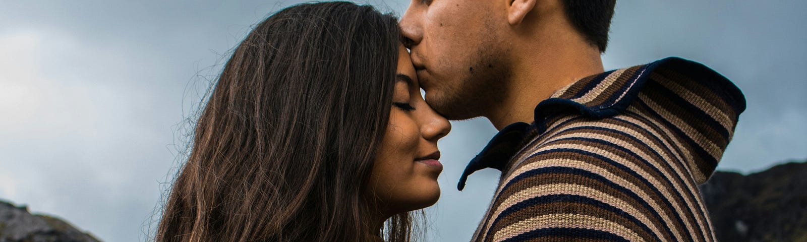 A man kissing on the forehead of another woman.