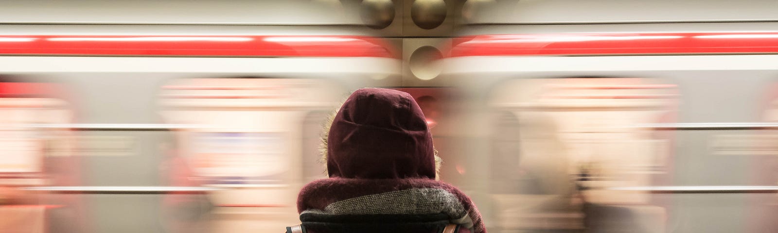 A woman waiting for a train while a different train whizzes by her.