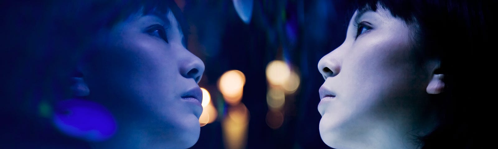 A woman at an aquarium looking at fishes in a tank. Cast in bluish light.