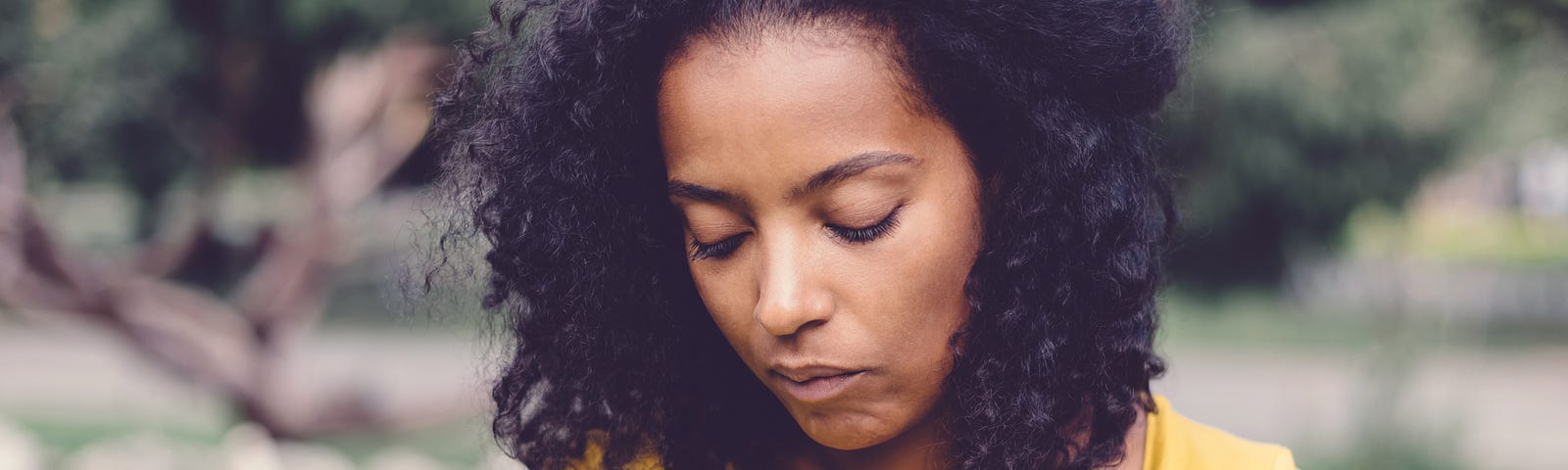 An anxious woman looks down while at the park.