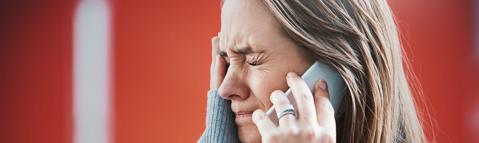 A young woman grimaces, her hand to her face as she hears something on the phone, obviously bad news.