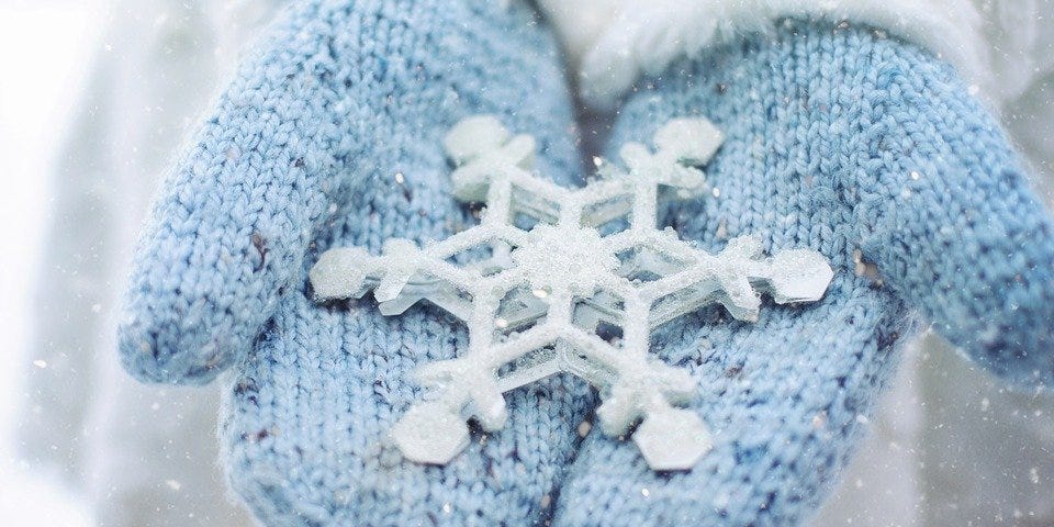 A pair of blue mittens holding a snowflake ornament.
