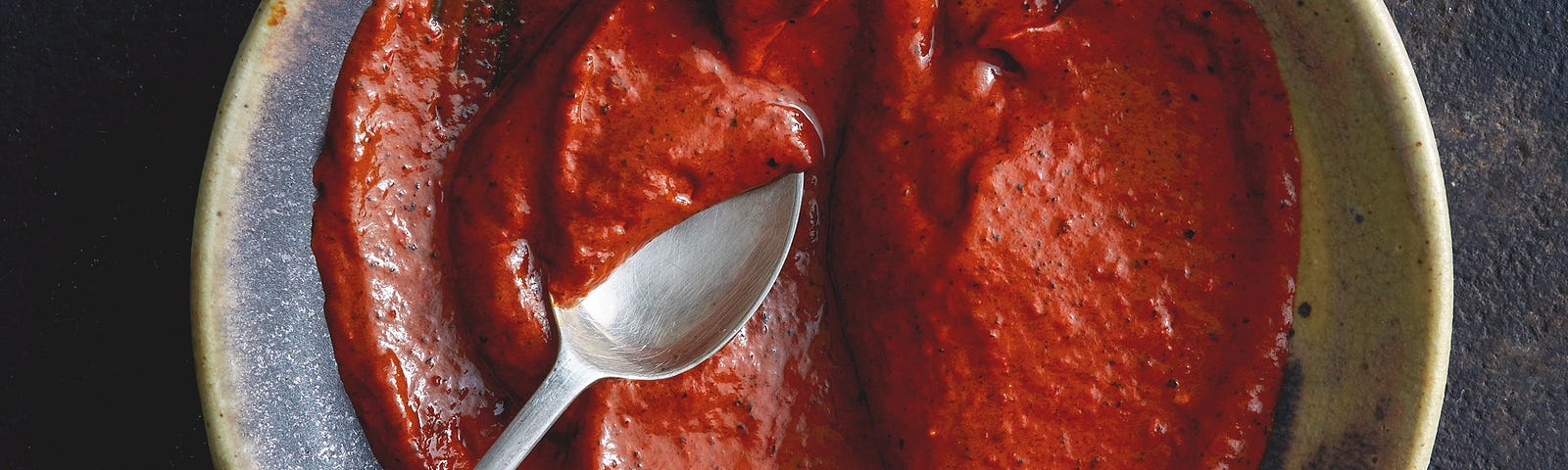 Overhead shot of a brown ceramic bowl with chile paste and a spoon in it.