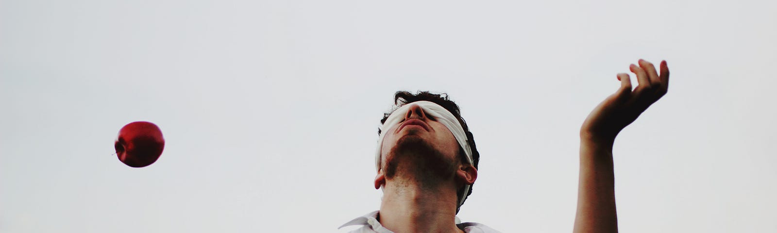 A man juggles 4 apples in the air while blindfolded.