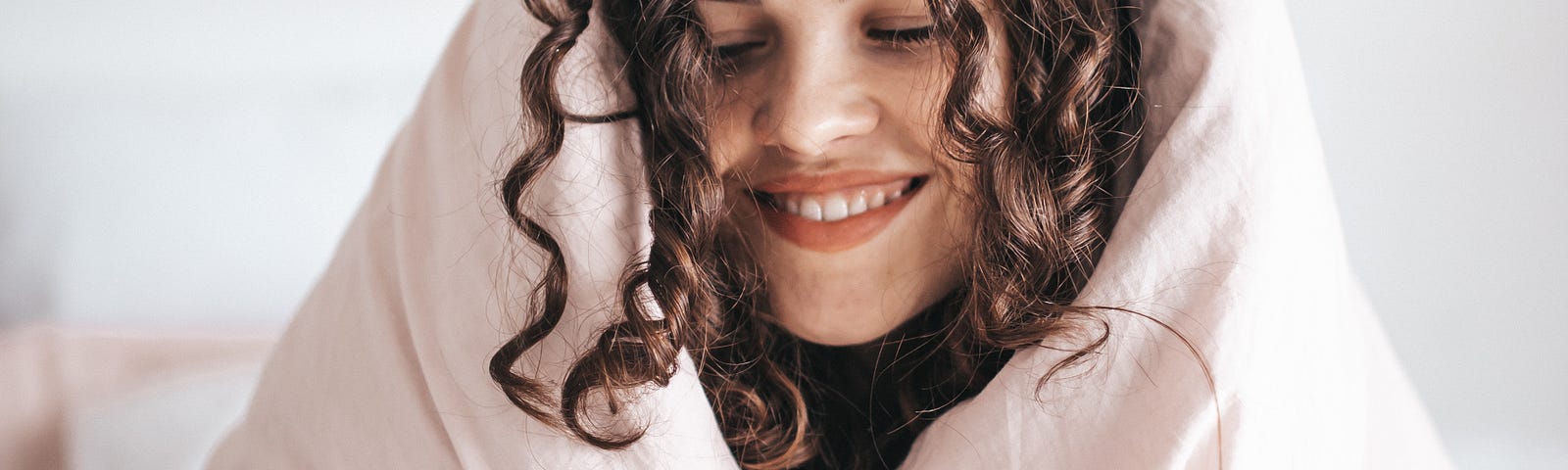 Smiling woman wrapped in a pink blanket, doing “self care”.