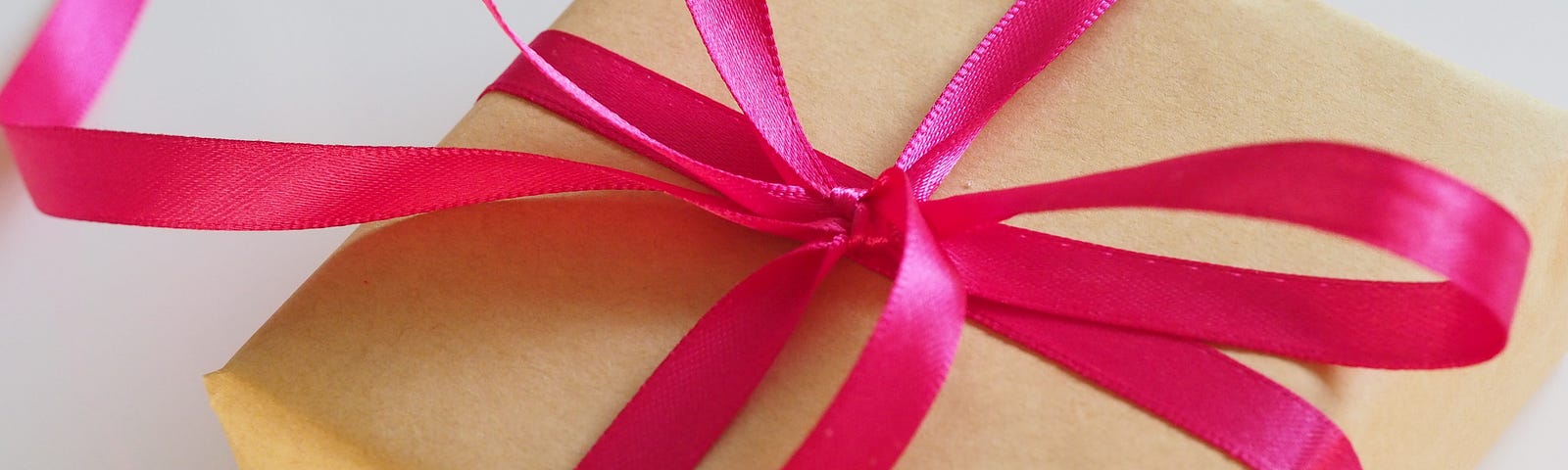 A gift box wrapped in brown paper and tied with a bright red ribbon