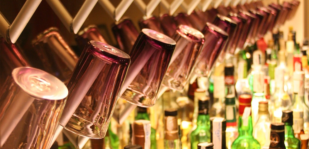 Rows of purple glasses hanging off the wall of a bar, with many liquor bottles below them.