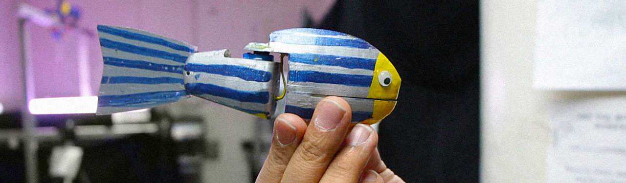Closeup of a hand holding a small robot that‘s been hand painted with blue stripes and has googly eyes glued on.