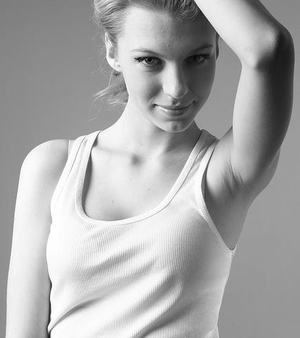 Attractive young woman wearing a white singlet, smiling, hand on head