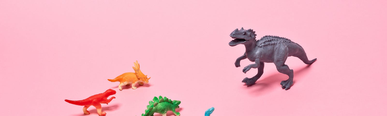 A photo of smaller dinosaur figurines in front of a T-rex figurine.