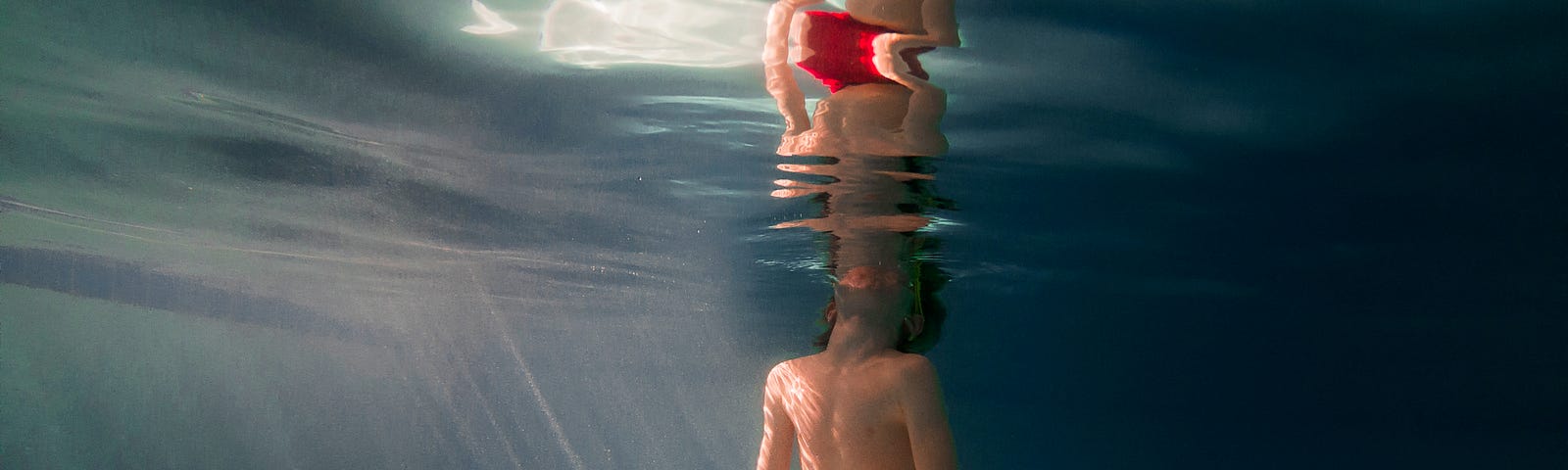 Underwater view of a boy in a swimming pool in the sunlight.