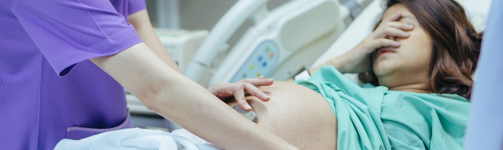 A doctor examines the belly of an expectant mother in the hospital room.