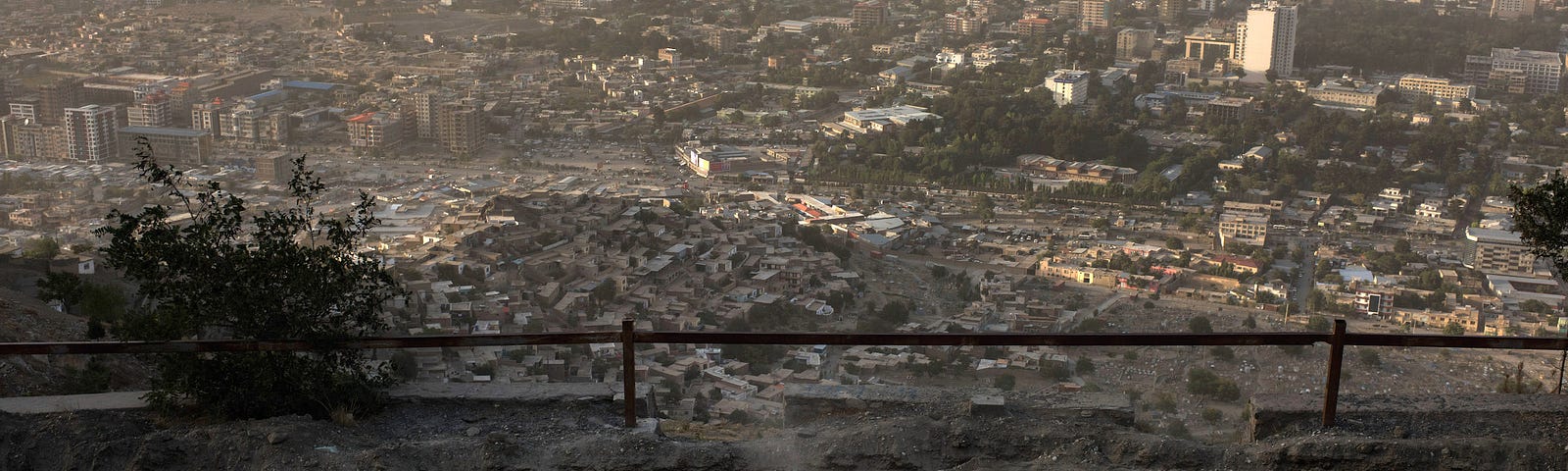 Children playing soccer in front of the dense, sprawling city of Kabul, haze and mountains in the distance.