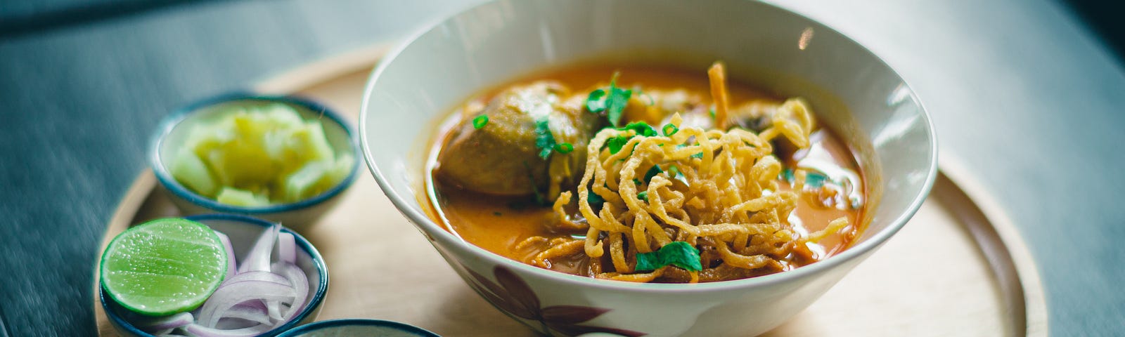 A bowl of ramen soup with dipping bowls of soy sauce, sliced onions, and other condiments.