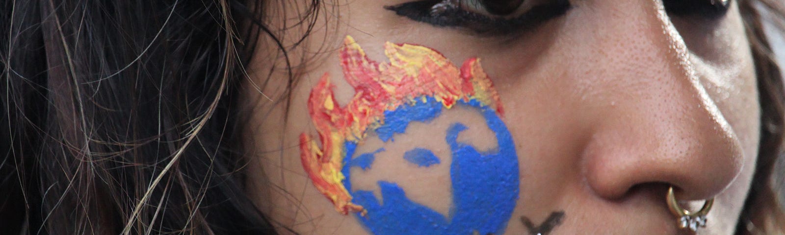 A close-up of a woman’s face with a painted drawing that says “Global Warning.”