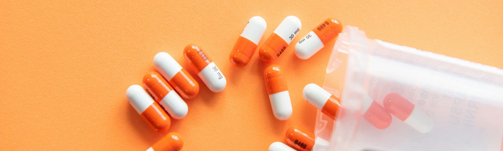 Prescription drugs on an orange background with a pill bottle.
