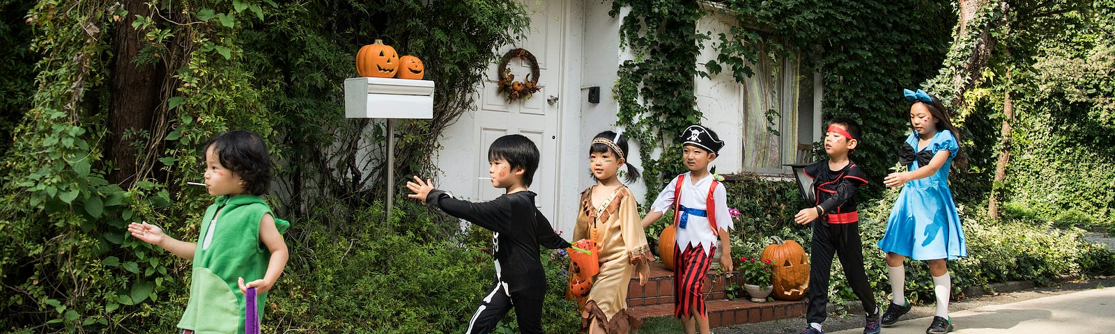 Children in Halloween costumes marching in a single-file line. The kid in the middle is dressed as a Native American.