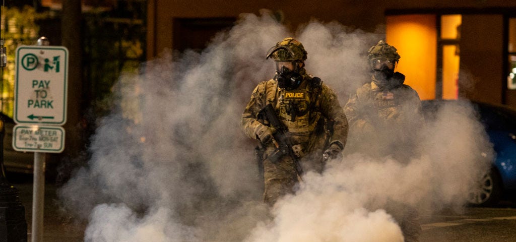 Federal officers in camoflague walk amidst tear gas while quelling protestors in Portland.