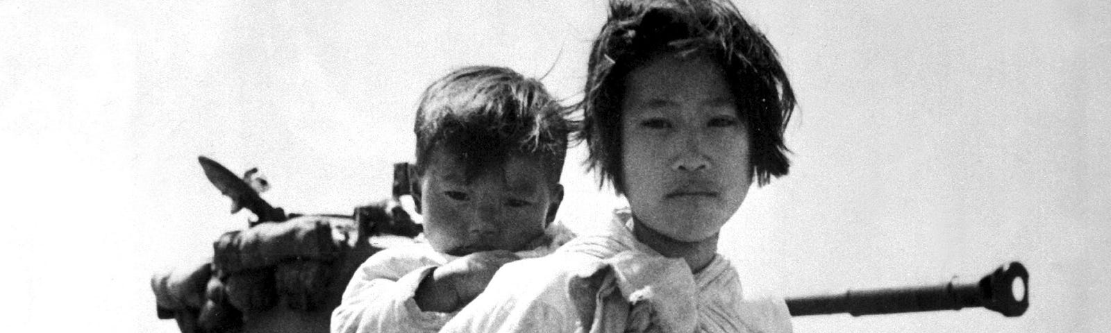 An archival photo from the Korean War. Carrying her baby brother on her back, a war weary Korean girl walks by a stalled M-26 tank, at Haengju, Korea, June, 1951.