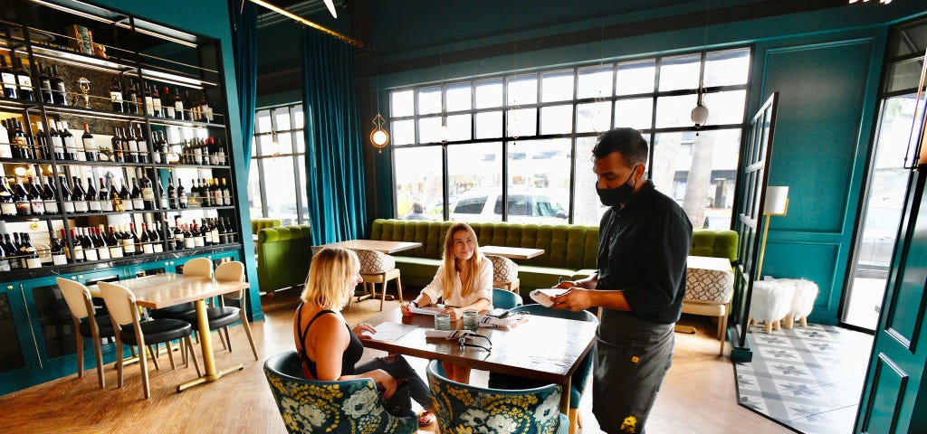 A server wearing a mask takes an order from two women at a restaurant in Orange County.